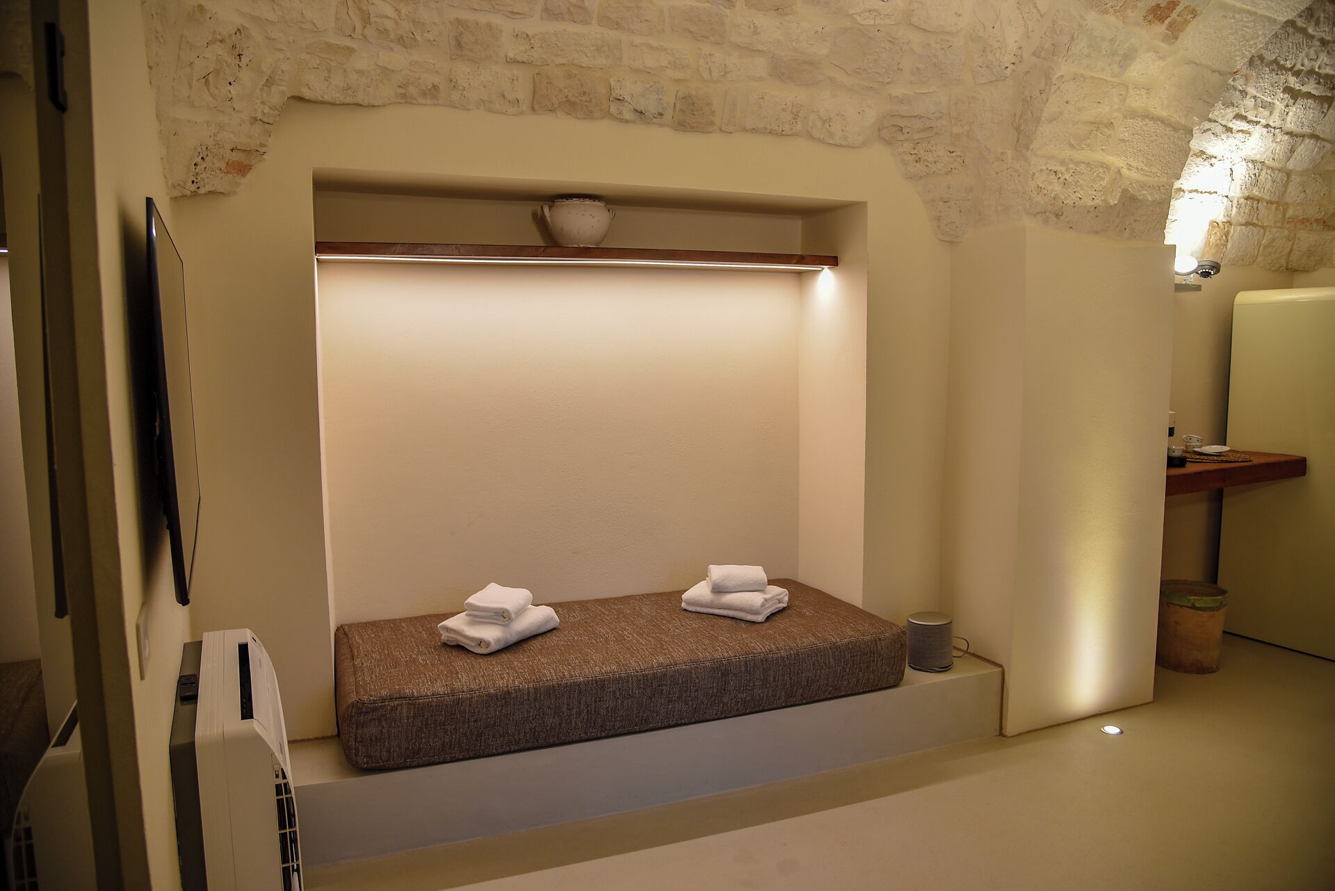 A small, cozy room with a bench, a wall-mounted shelf, and a light fixture.