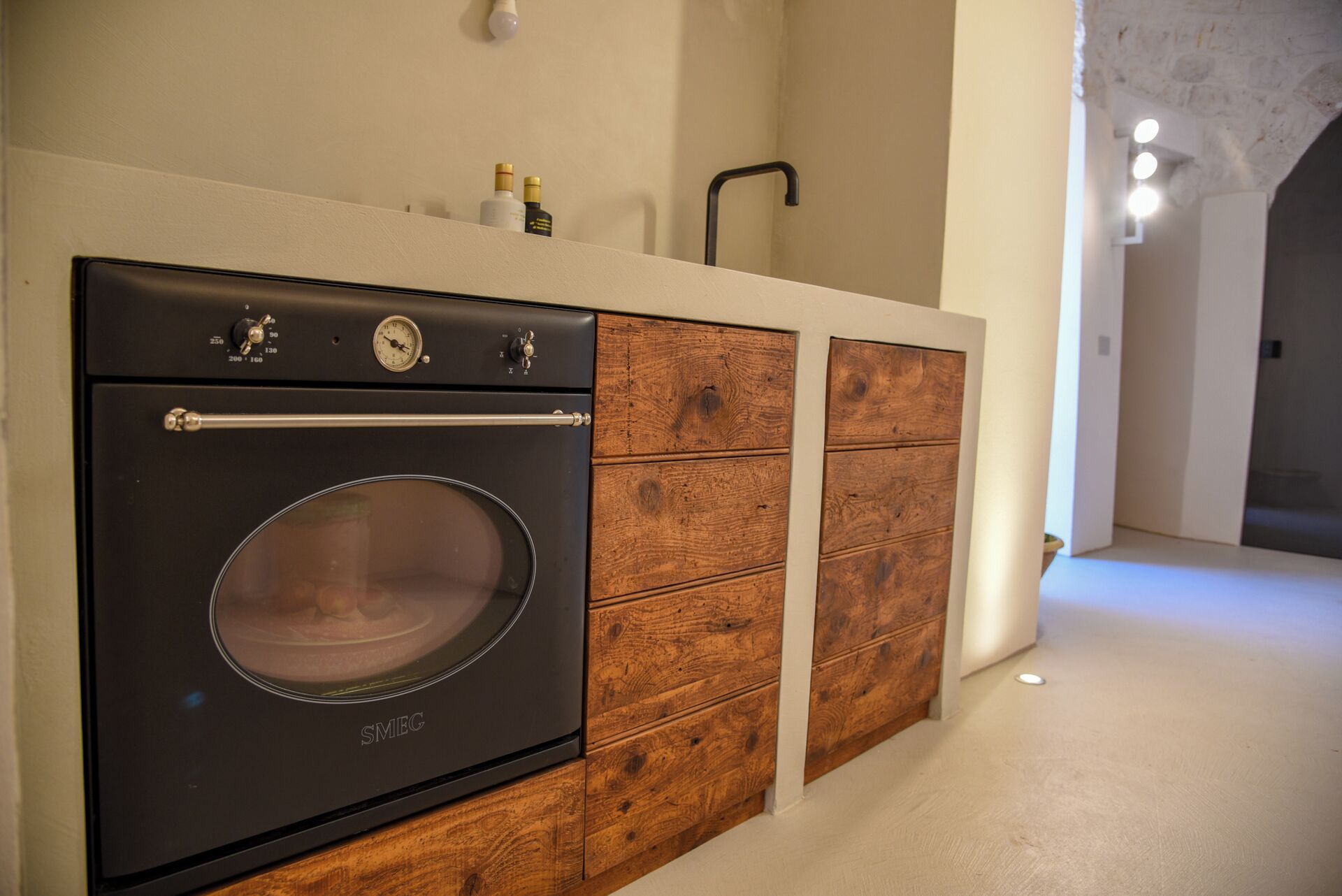 Cocina con horno moderno, armarios de madera y encimera con botellas.