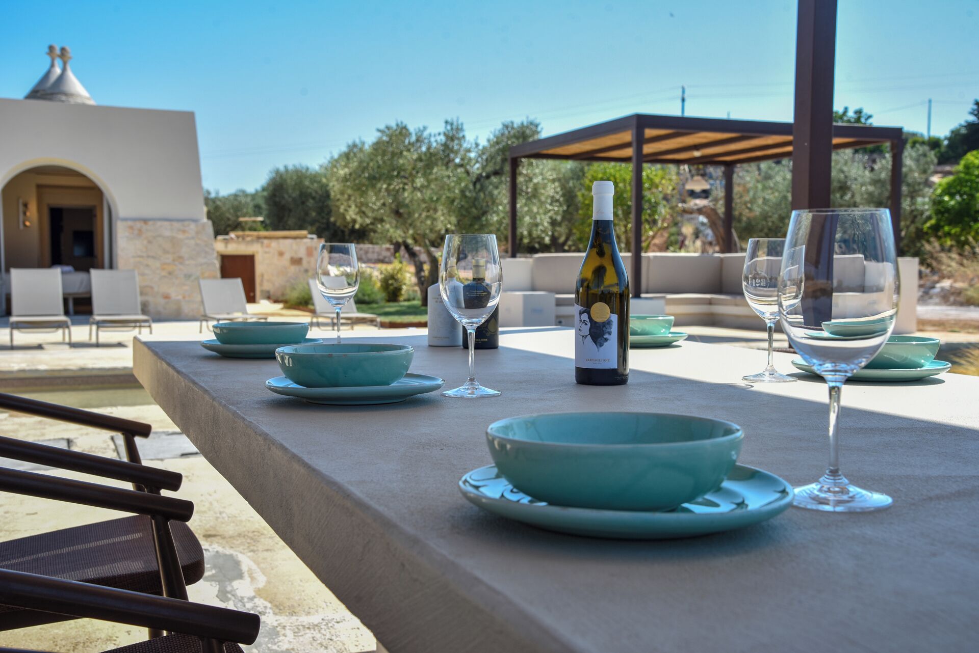 Un área de comedor al aire libre con una mesa dispuesta para dos personas, una botella de vino y vistas del paisaje circundante.