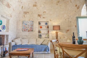Una habitación rústica con paredes de piedra, un sofá, una mesa de madera, una estantería y una lámpara.