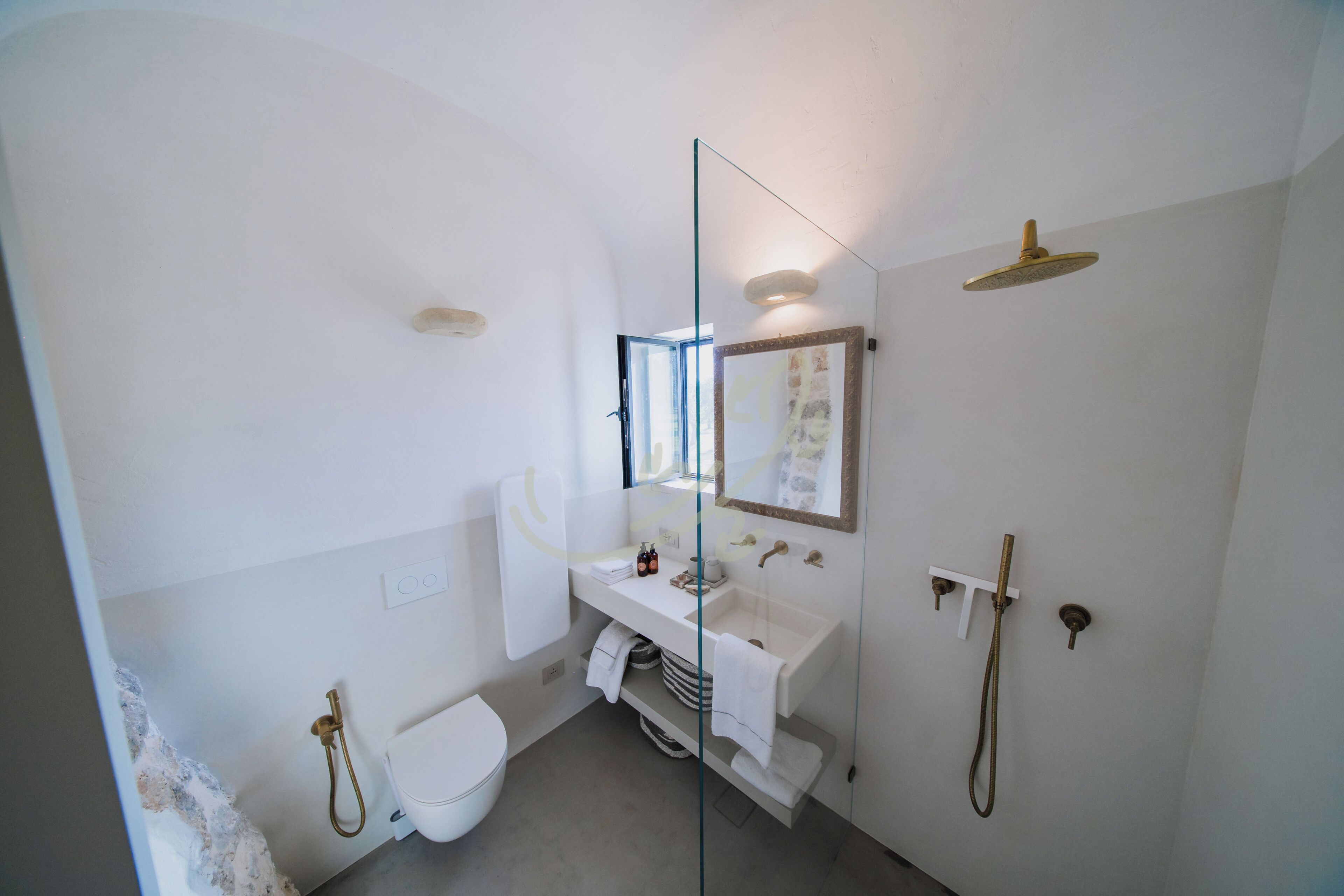 A modern bathroom with a glass partition, a white sink, a toilet, and a shower area.