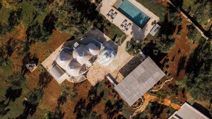 An aerial view of a property with a swimming pool, outdoor seating area, and a dome-shaped structure. - TD Trullo Lumina Boutique Luxury Trulli With Pool (Ostuni)