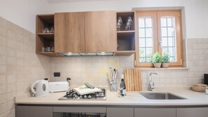 A modern kitchen with wooden cabinets, a built-in oven, a sink, and a window with plants. - TD Trulli Bruco Large Pool for Family Fun (Monopoli)
