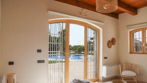 A hotel room with a bed, a window with a view of a swimming pool, a wicker chair, and a radiator. - TD Trulli Bruco Large Pool for Family Fun (Monopoli)