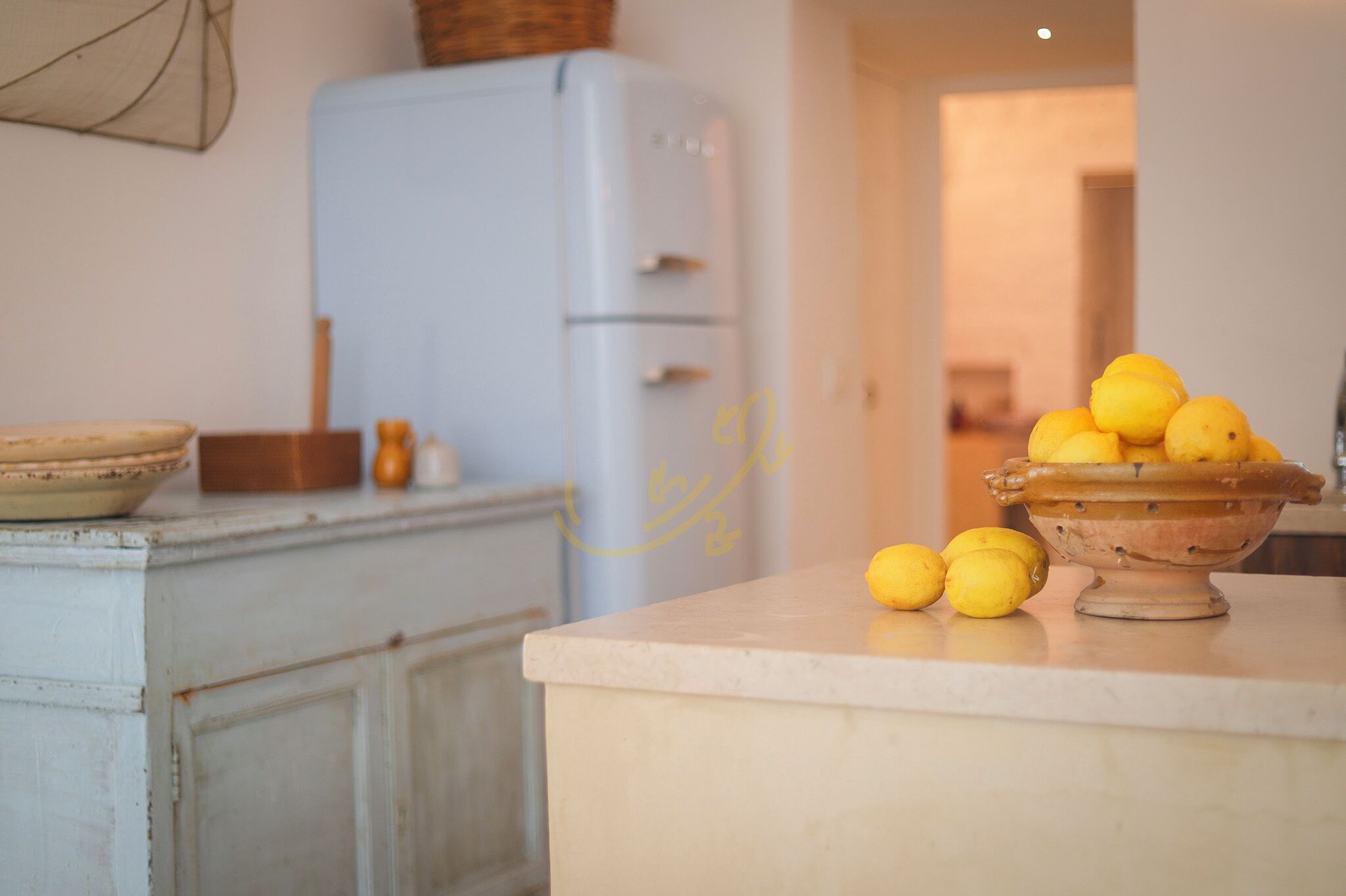 A kitchen with a white refrigerator, a bowl of lemons, and a wooden bowl on the counter.