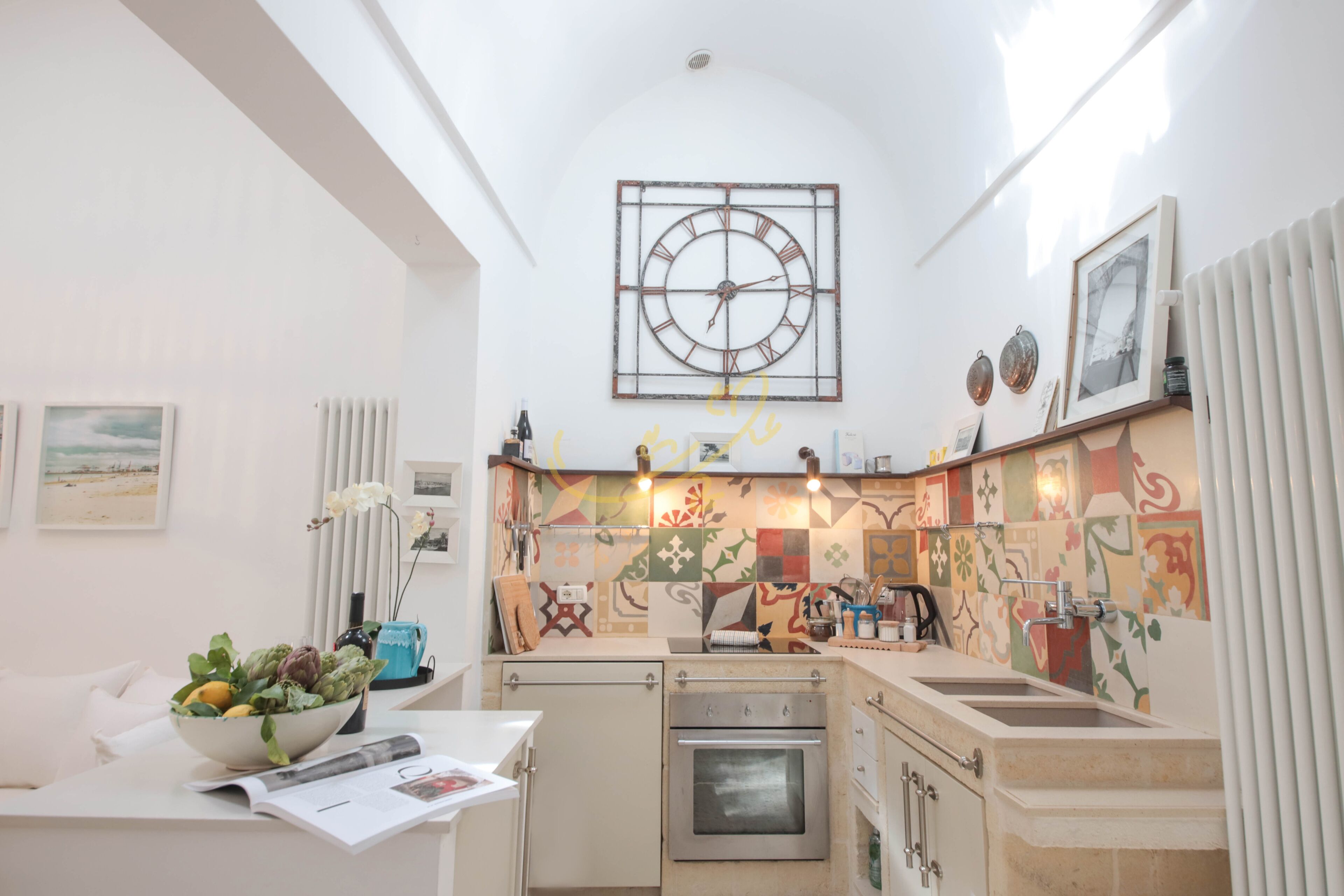 A compact kitchen with a central island, a built-in oven, and a wall-mounted clock.