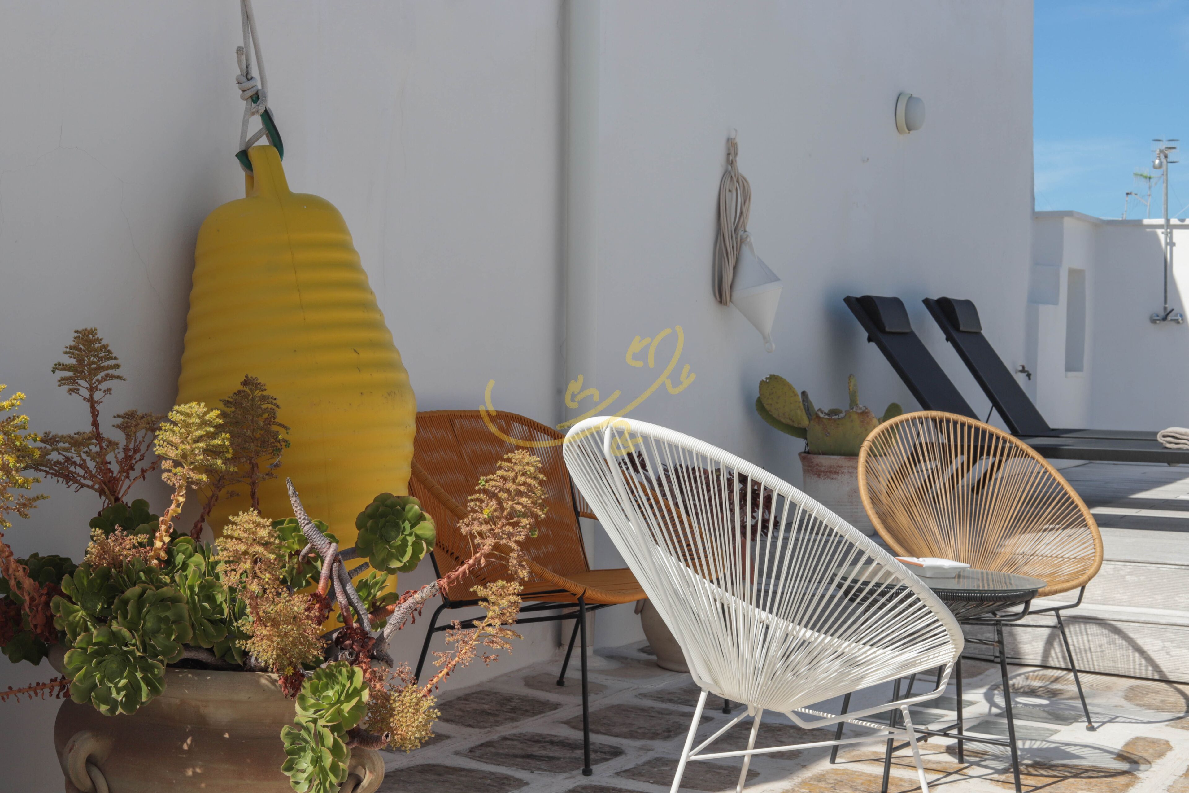A terrace with wicker chairs, a yellow bottle sculpture, and a potted plant.