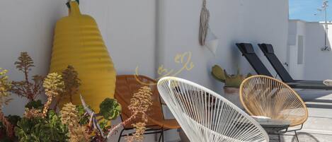 A terrace with wicker chairs, a yellow bottle sculpture, and a potted plant.