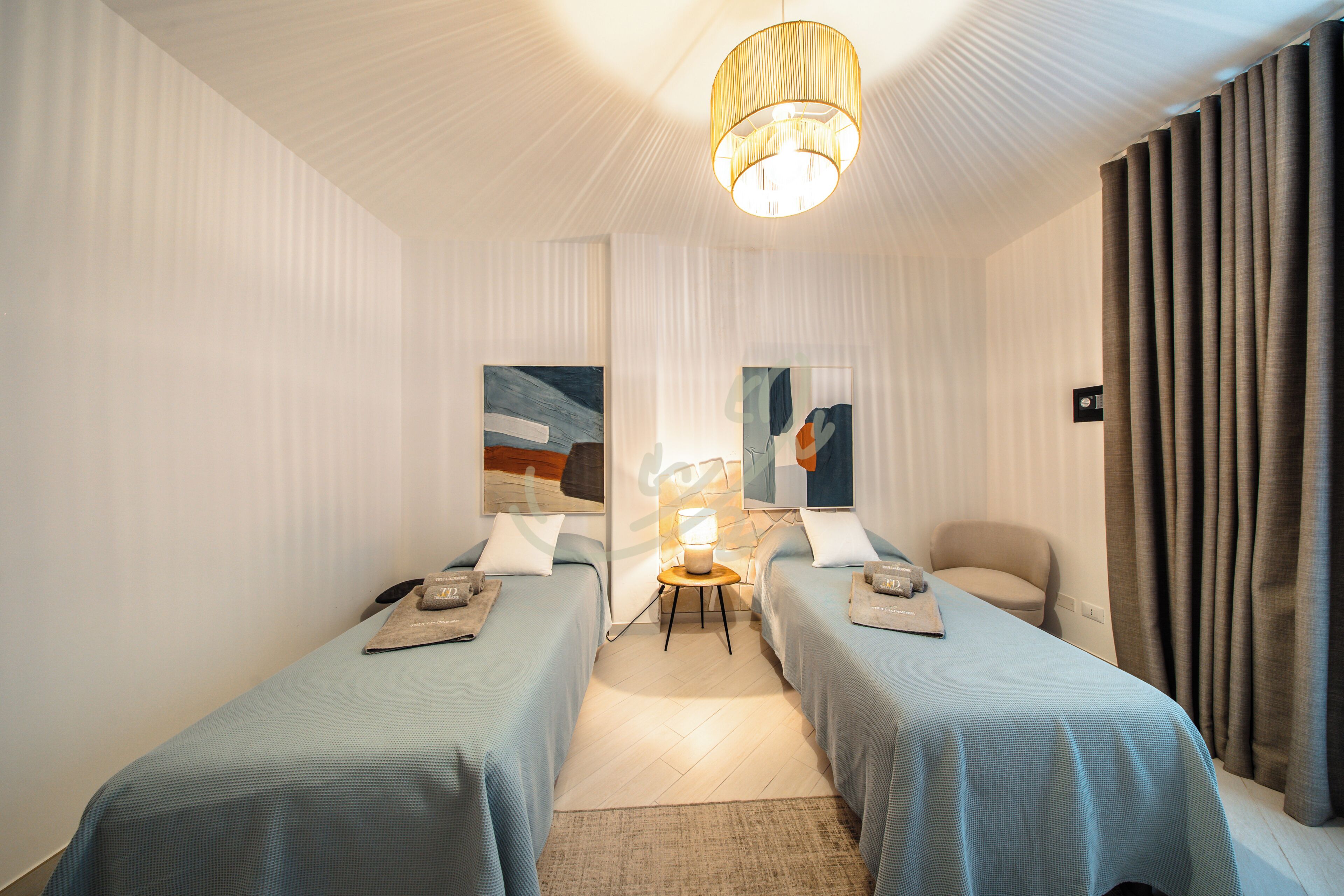 A hotel room with two beds, a lamp, a chair, and artwork on the walls.