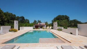 A rectangular swimming pool with a clear blue water surface, surrounded by a tiled deck. There are lounge chairs with towels on them, and a building with a sloped roof in the background. - TD Casale Belladinotte Poolside Country Bliss (Ceglie Messapica)