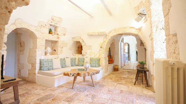 Un interno rustico con pareti in pietra, pavimento in pietra, un'area relax con cuscini, un tavolino e una chitarra.