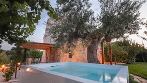 An outdoor swimming pool with a stone wall and trees in the background. - TD Torretta San Procopio Stone House With Pool (Castellana Grotte)