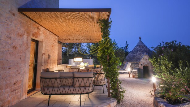 An outdoor patio with a dining area, stone walls, and a small stone structure. - TD Torretta San Procopio Stone House With Pool (Castellana Grotte)