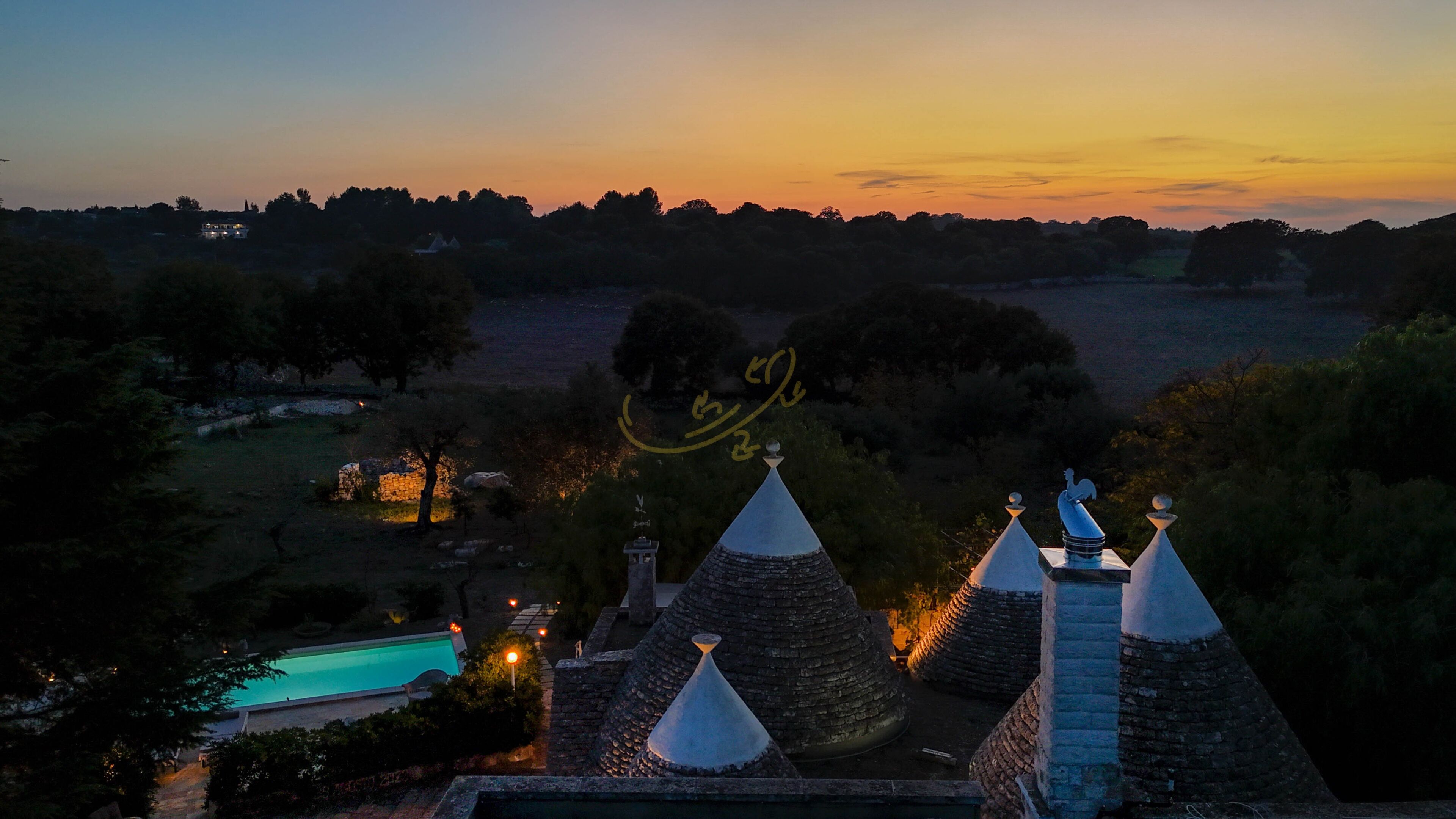 A building with multiple pointed roofs, a swimming pool, and a view of the surrounding landscape at dusk.