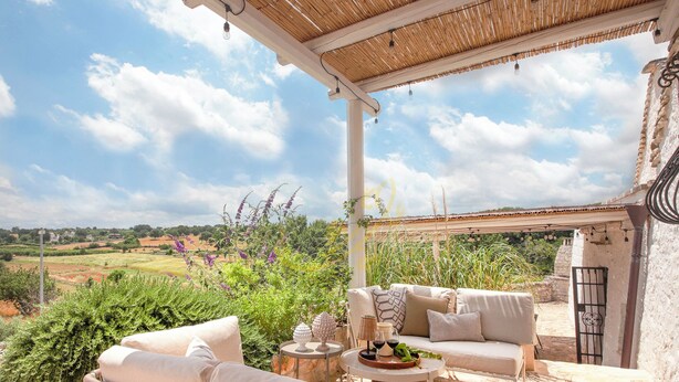A covered outdoor seating area with wicker furniture, a table with a wine bottle, and a view of the countryside. - TD Trulli Altura With Pool & Stunning Sunsets (Martina Franca)