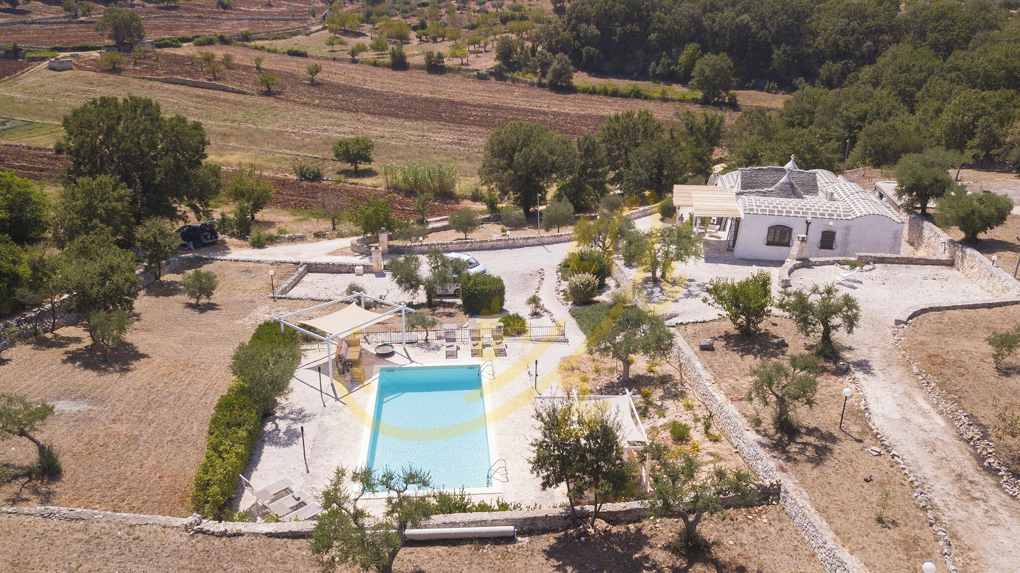 An aerial view of a property with a swimming pool, a patio area, and a house with a tiled roof.