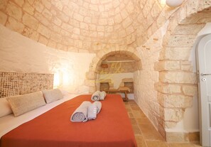 Ein Zimmer mit Steinwänden, einem Bett, Handtüchern und einer Bank.