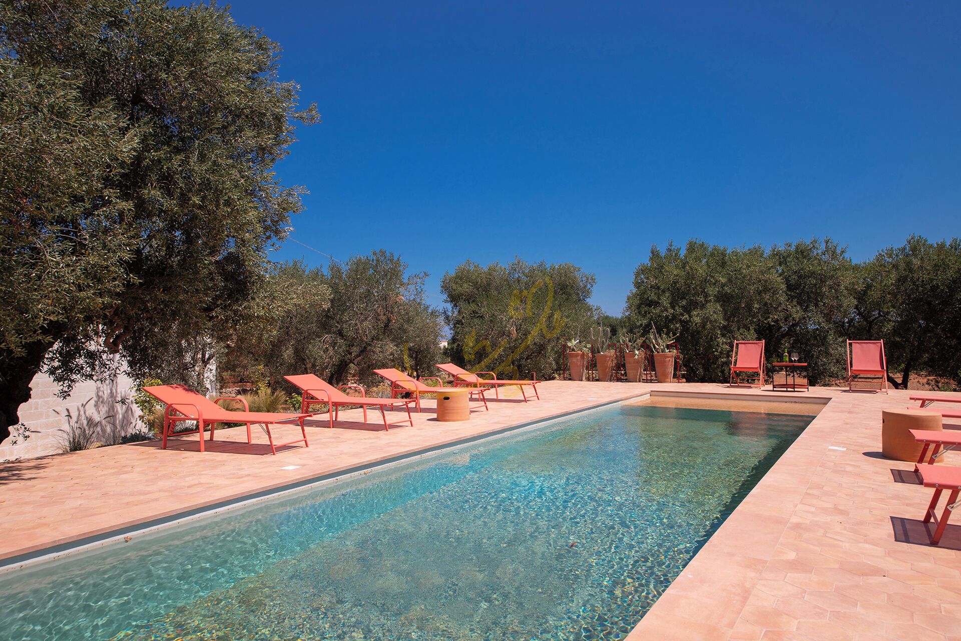 A clear swimming pool with sun loungers and potted plants around it.