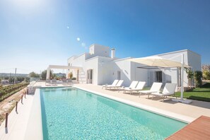 A modern poolside area with a clear blue pool, white lounge chairs, and a covered seating area. - TD Tenuta Donna Madia Sea View Pool Over Vineyard (Monopoli)