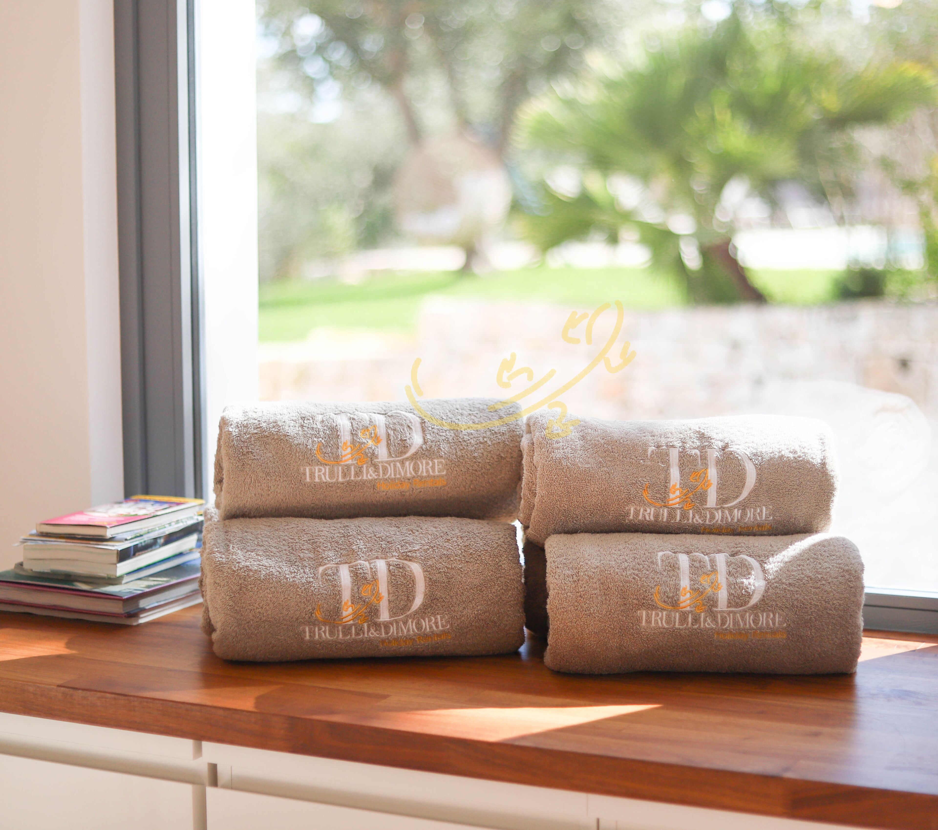 Une pile de serviettes ornées de motifs brodés, posée sur une surface en bois près d’une fenêtre.