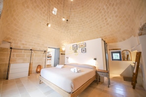 A bedroom with a brick ceiling, a bed with white linens, a wooden bedside table, a mirror, and a picture on the wall.