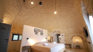 A bedroom with a stone ceiling, a bed, a bedside table, a small stool, and a wall-mounted TV. - TD Trulli Tortorella With Nature Pool & Sauna (Monopoli)