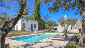 A swimming pool with lounge chairs, a white building, and stone structures in a landscaped garden. - TD Trulli Tortorella With Nature Pool & Sauna (Monopoli)