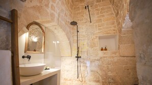A bathroom with a stone wall, a round sink, a mirror, and a shower. - TD Trulli Tortorella With Nature Pool & Sauna (Monopoli)