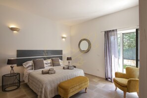 A bedroom with a bed, bedside lamps, a round mirror, a yellow armchair, and a view of the outdoors through a window. - TD Villa Coco Countryside Villa Near Ostuni (Ostuni)