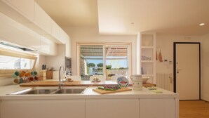A modern kitchen with white cabinetry, a central island with a sink, and a view through a large window.