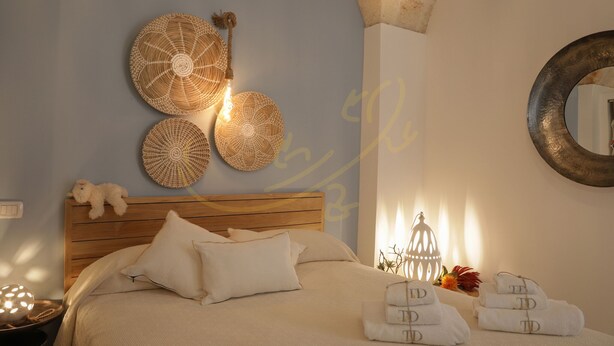 Un letto rifatto con cura, una testiera in legno, un punto luce decorativo a parete e uno specchio.