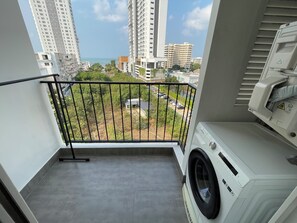 Ein Balkon mit Waschmaschine, Blick auf einen Parkplatz und hohe Gebäude im Hintergrund.