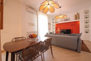 A dining area with a wooden table and wicker chairs, a grey sofa, and a red accent wall with a television. - TD Sesto Piano With Sea View Living Terrace (Monopoli)