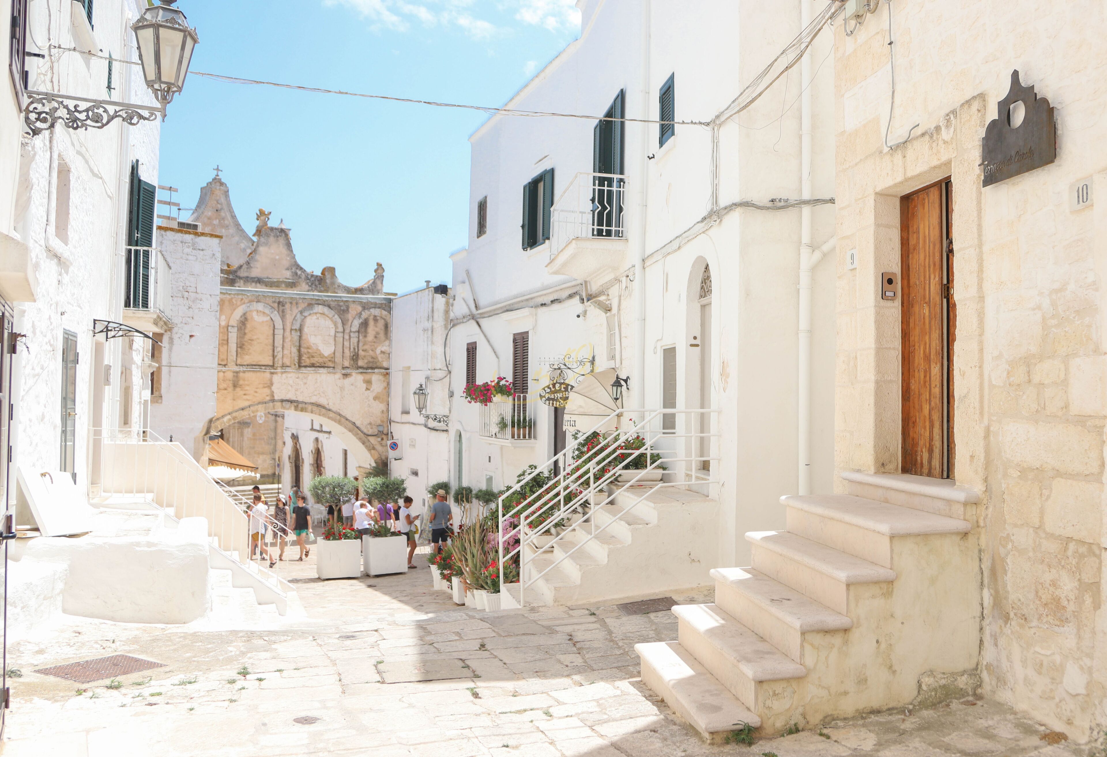 A narrow street with white buildings, a staircase, and a church in the background.
