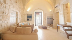 A cozy living room with a stone wall, a sofa, ottomans, and a wooden table. - TD Terrazze di Carole Panoramic Terrace & Jacuzzi (Ostuni)
