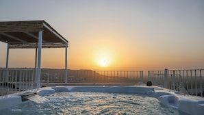 A hot tub with a wooden deck and metal railing, overlooking a sunset and distant hills. - TD Terrazze di Carole Panoramic Terrace & Jacuzzi (Ostuni)
