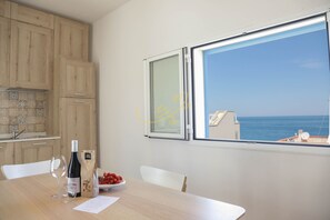 A kitchen with wooden cabinets, a window with a view of the sea, a wine bottle, and a bowl of fruit. - TD Casa Marevino Seaside Terrace W/panoramic View (Polignano a Mare)