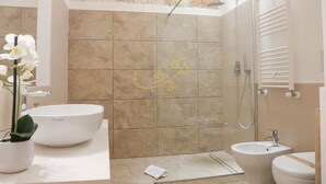 A modern bathroom with a large white sink, a bidet, and a shower area.