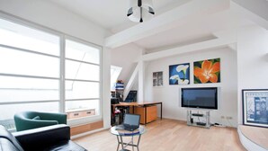 Uma sala de estar moderna com um sofá de couro preto, uma mesa de centro de vidro, uma televisão e obras de arte nas paredes.