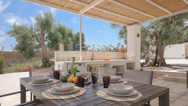 Un espacio de comedor al aire libre con una mesa dispuesta para cuatro personas, rodeado por una pérgola.