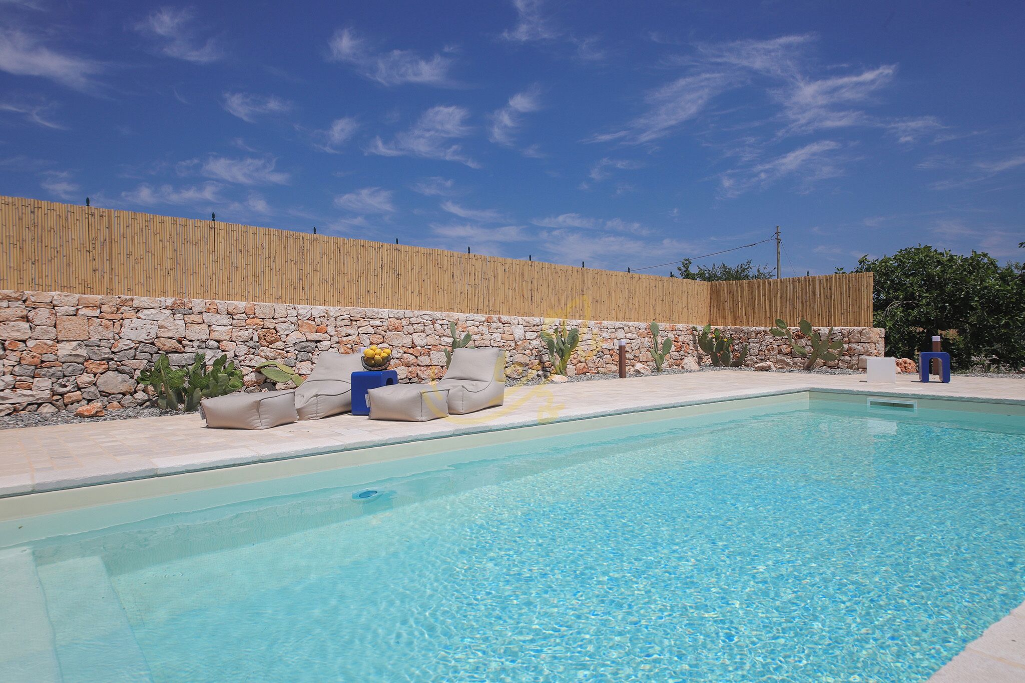 A swimming pool with a stone wall and a bamboo fence in the background.
