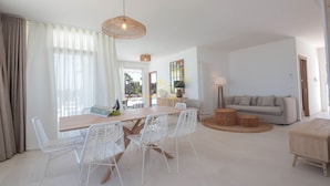 Un salon moderne avec une table à manger en bois, des chaises en osier blanches, un canapé gris et une table basse en bois.