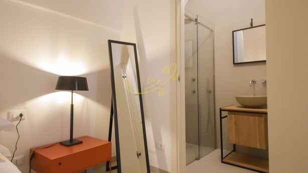 A modern bathroom with a glass shower, a wooden vanity, and a bedside table with a lamp. - TD Trullo Morena Charming Trullo,stunning Sunsets (Monopoli)