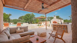 An outdoor patio with a wooden ceiling, a stone fireplace, and a pool in the background. - TD Trullo Titiro Vineyard, Wine Cellar & Pool (Ostuni)
