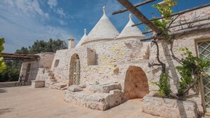 A stone building with conical roofs, a staircase, and a small table with chairs. - TD Trullo Titiro Vineyard, Wine Cellar & Pool (Ostuni)