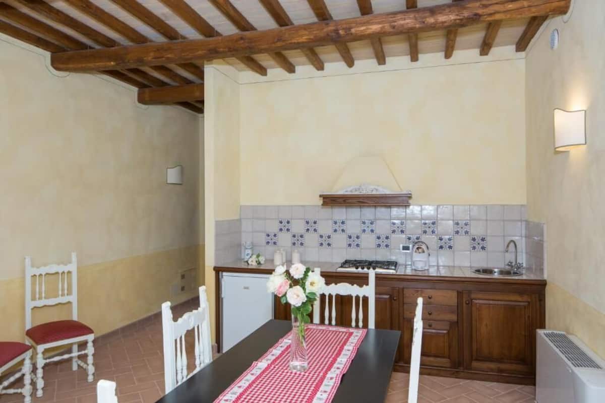A kitchen with a tiled backsplash, wooden cabinets, a dining table with chairs, and a vase with flowers.