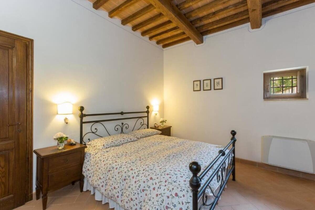A bedroom with a wooden ceiling, a bed with a metal frame, two bedside tables with lamps, and a window with a view.