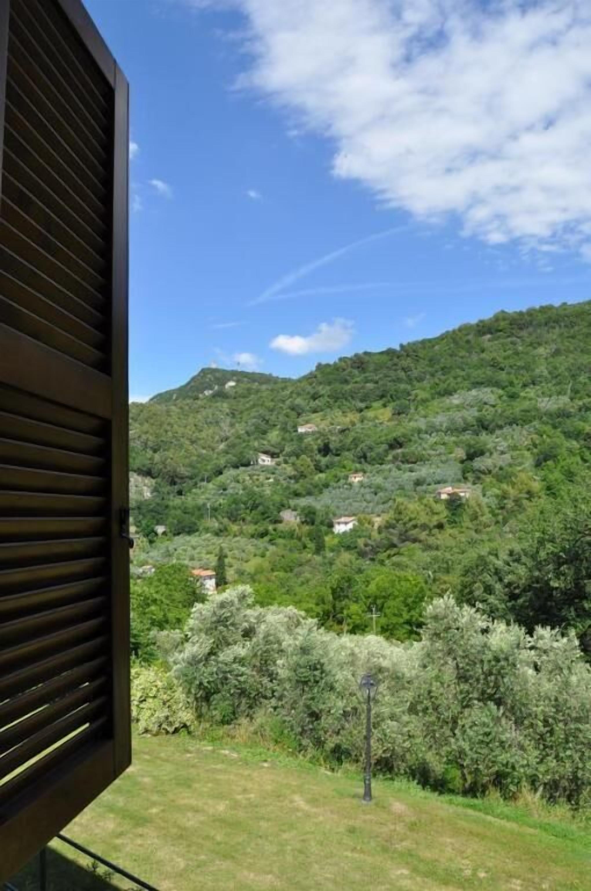 A view from an open window overlooking a hillside with scattered buildings and dense greenery.