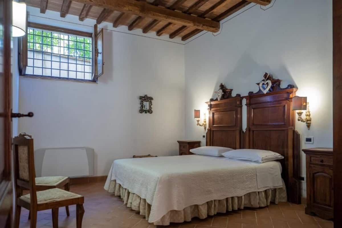 A bedroom with a bed, two bedside tables, a chair, a window, and a wooden ceiling.