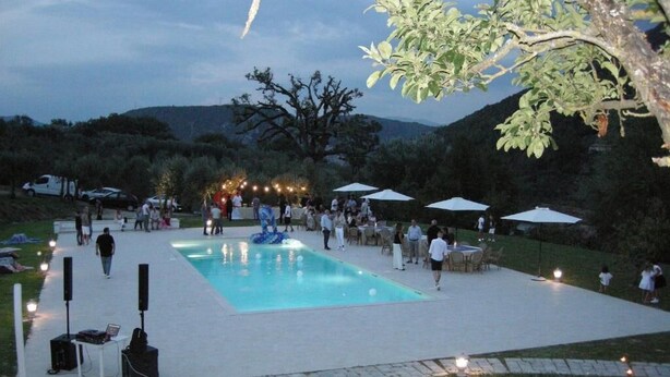 An outdoor pool area with a paved deck, surrounded by trees and hills in the background. - Agriturismo Il Borgo di San Michele (Terni)